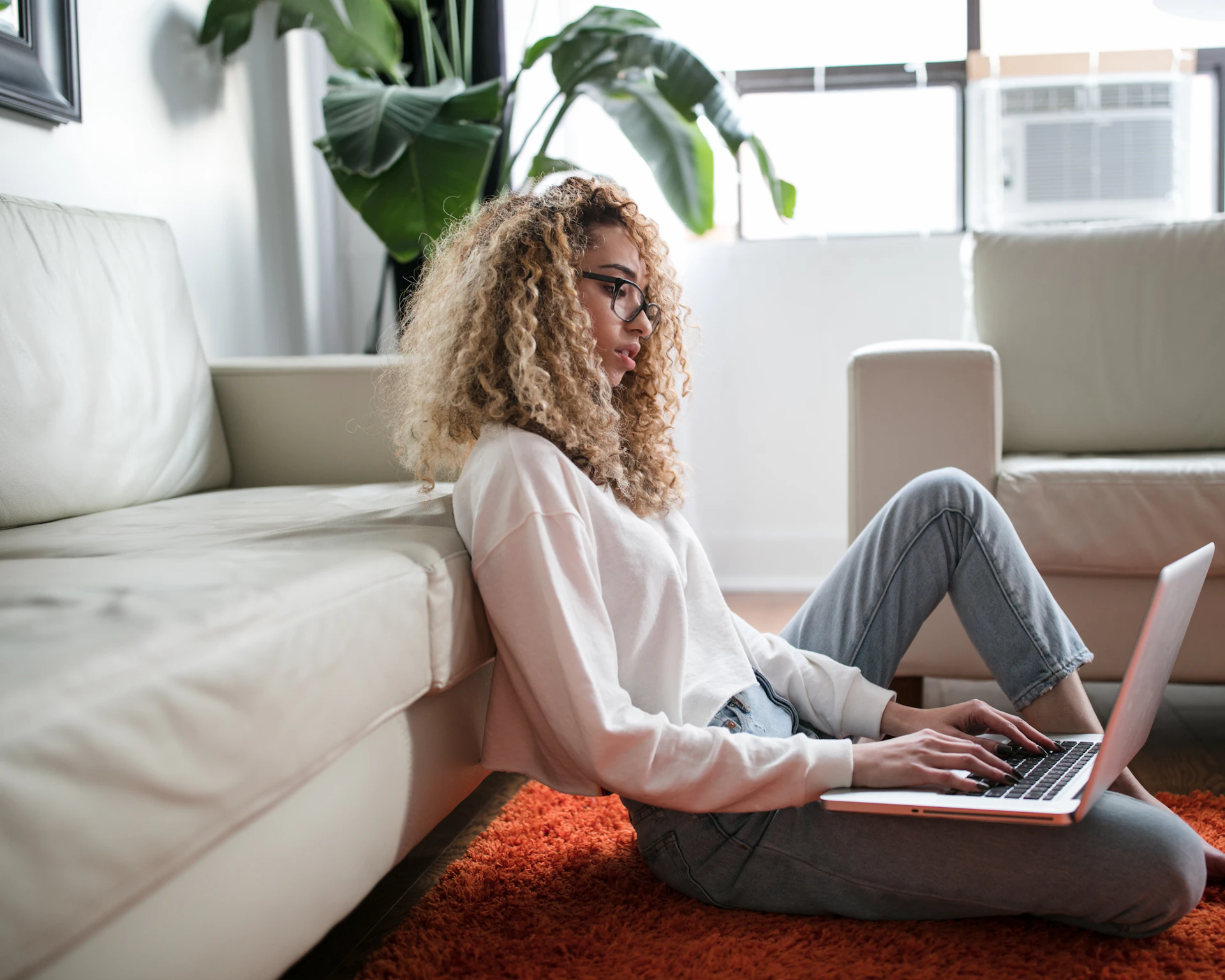 A woman sitting on the floor of her living room, using a laptop