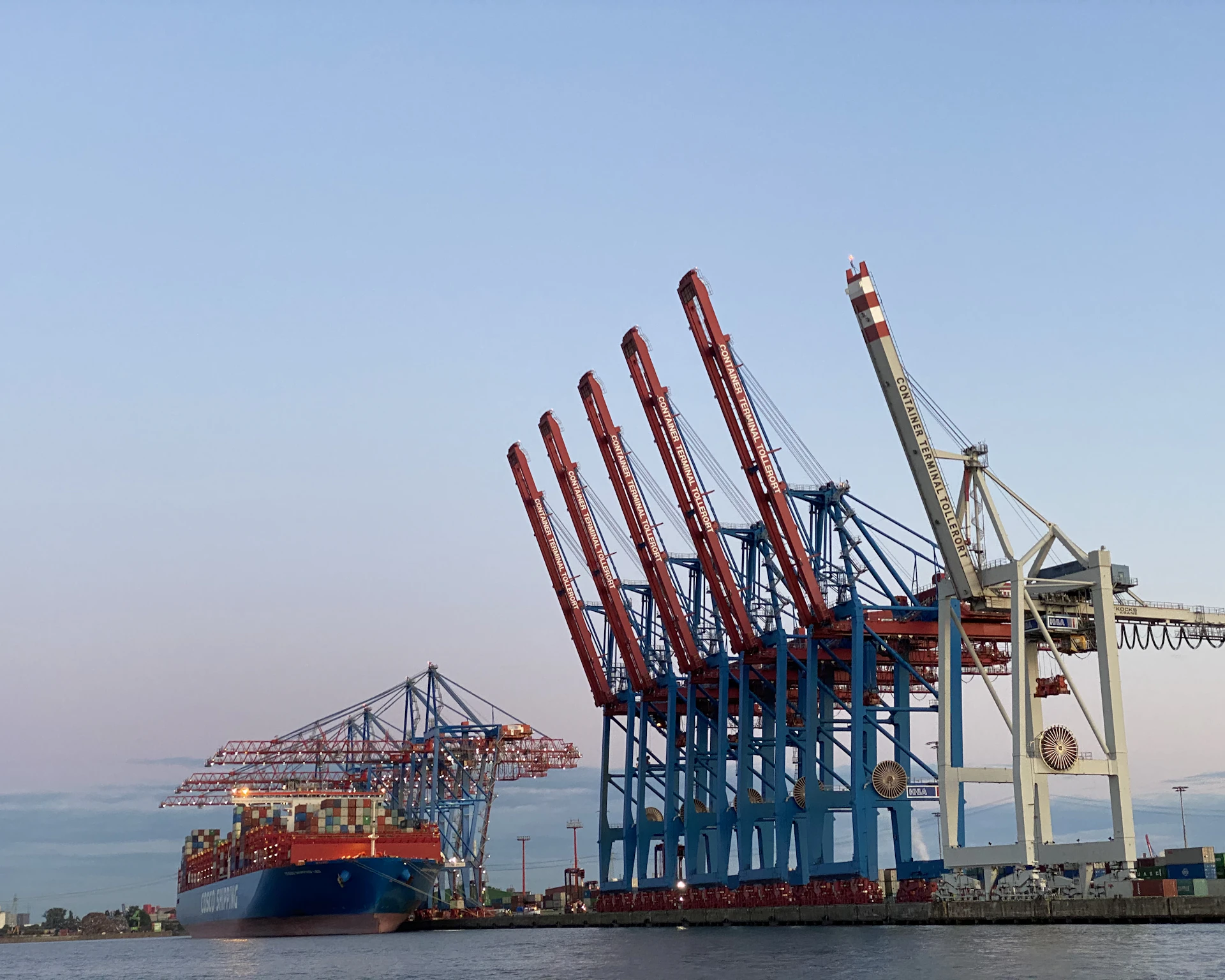 Container cranes and a cargo ship at a busy port under a clear sky