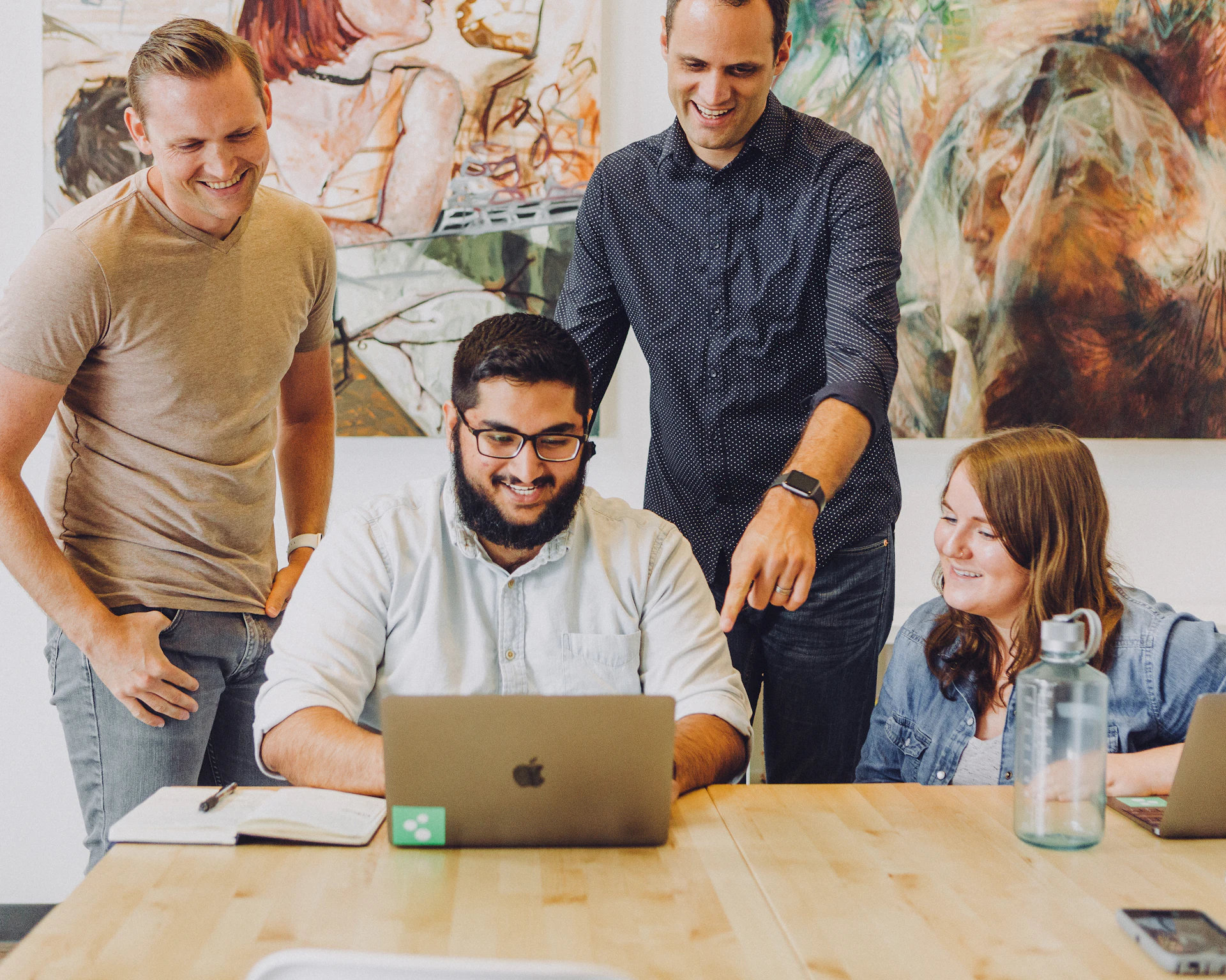 Four colleagues smiling around a laptop at a table