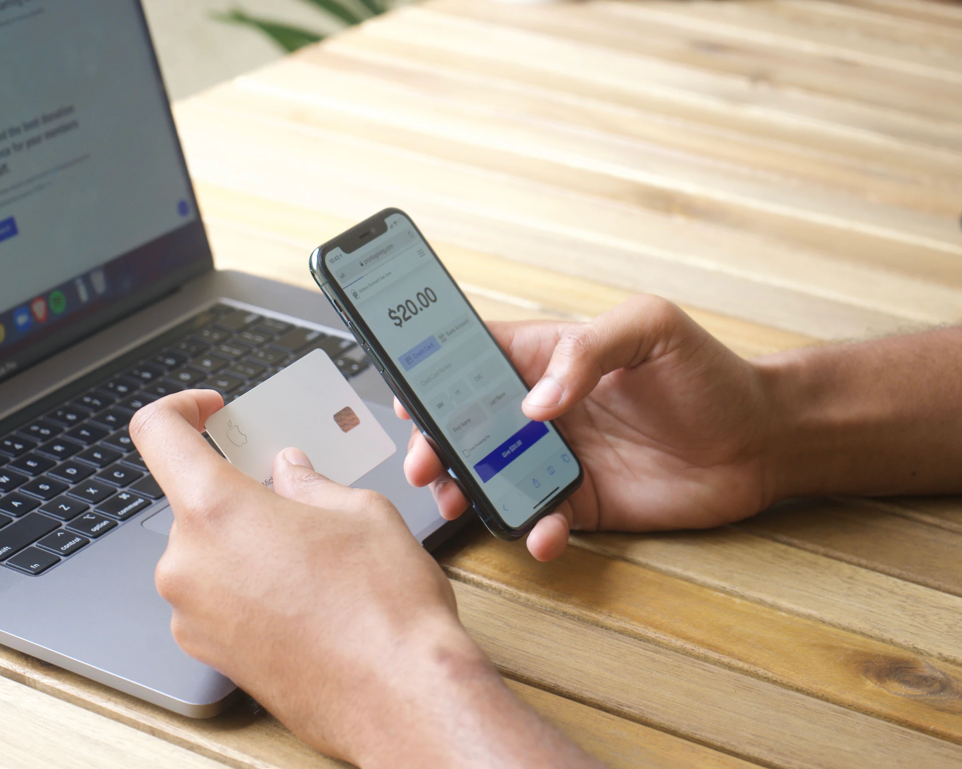 A person holding a phone and a bank card beside a laptop