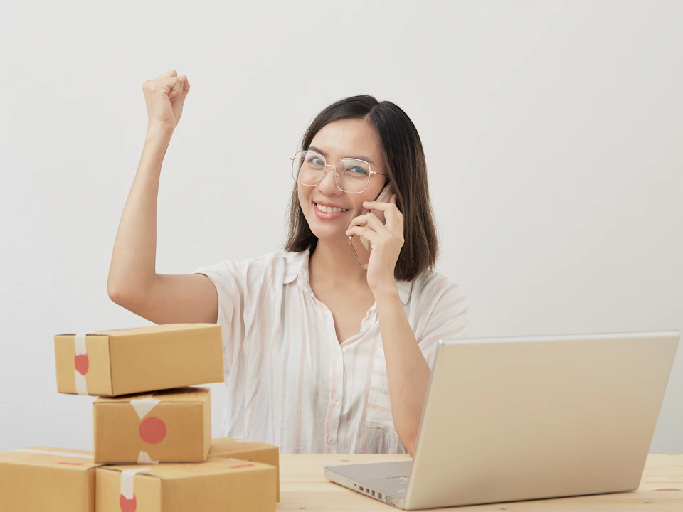 A woman celebrating beside parcels and a laptop