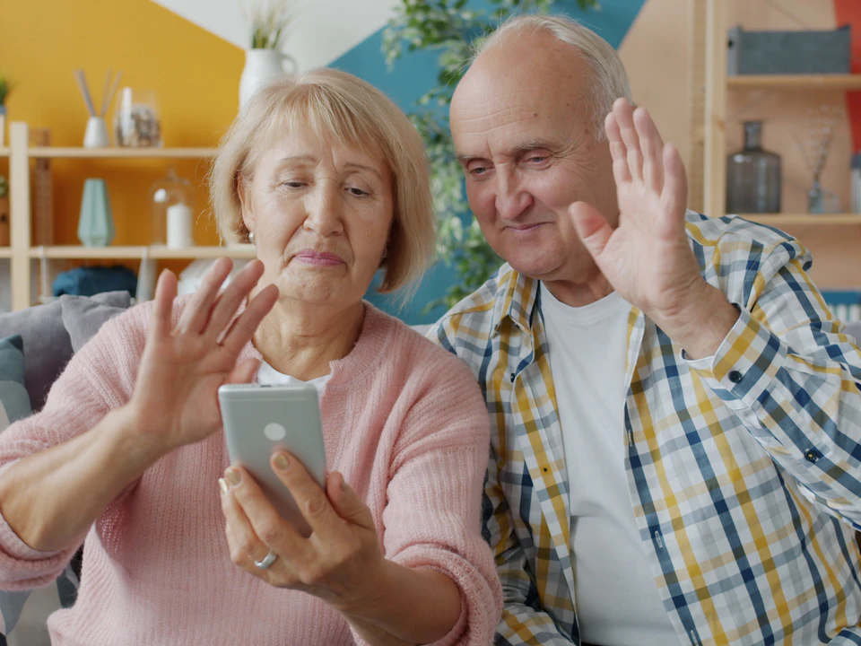 An older couple waving at a video call on a phone