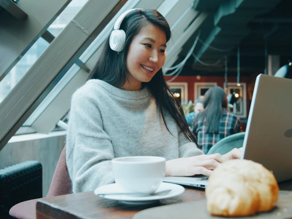 A woman with headphones working on a laptop in a café