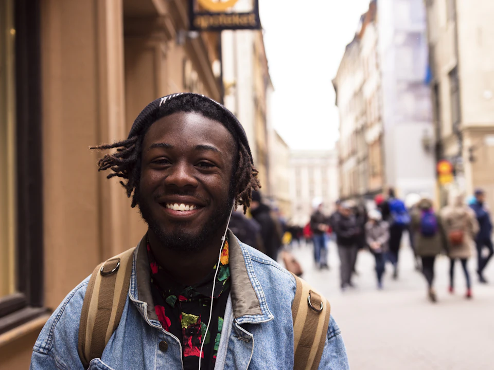 A smiling student with a backpack on a busy city street