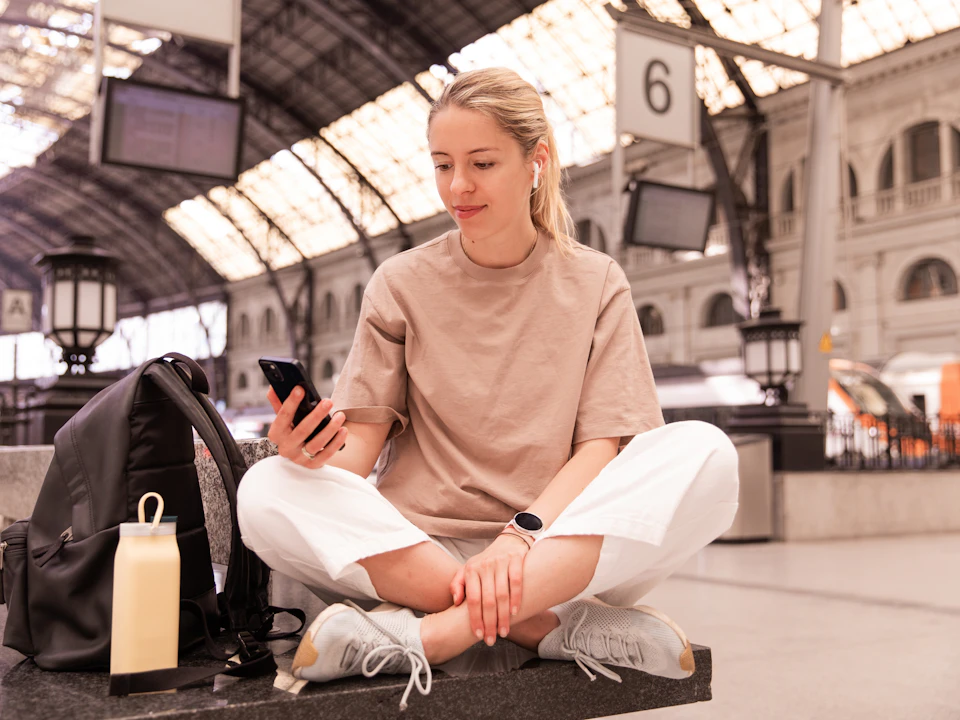 A woman sitting with her bag at a station, looking at her phone