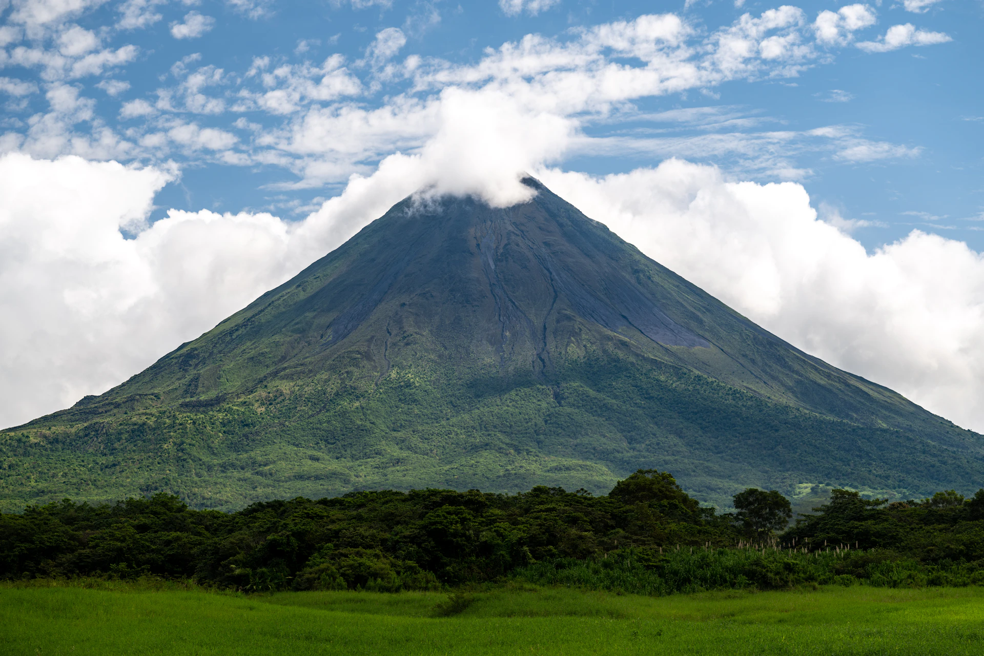 Il vulcano Arenal che si erge sopra campi verdi