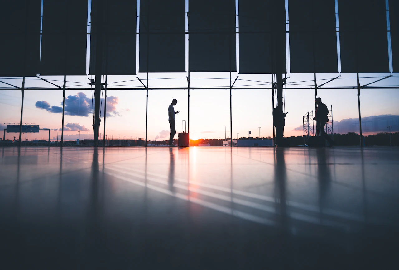 Travellers with luggage silhouetted against the windows of an airport terminal