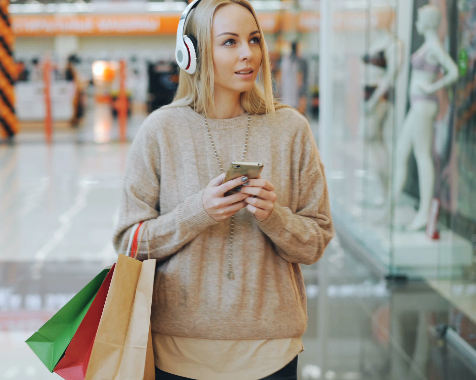 A woman with headphones and shopping bags checking her phone in a shopping centre